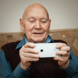 An older man playing Staying Sharp games from aarp.org on an iPhone as he smiles