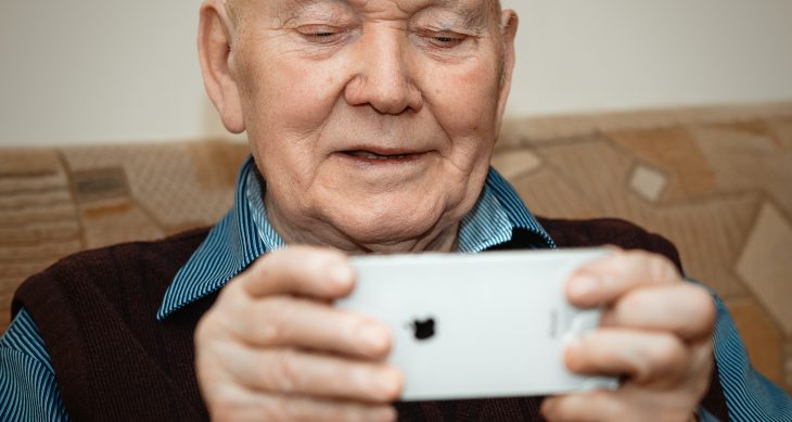 An older man playing Staying Sharp games from aarp.org on an iPhone as he smiles