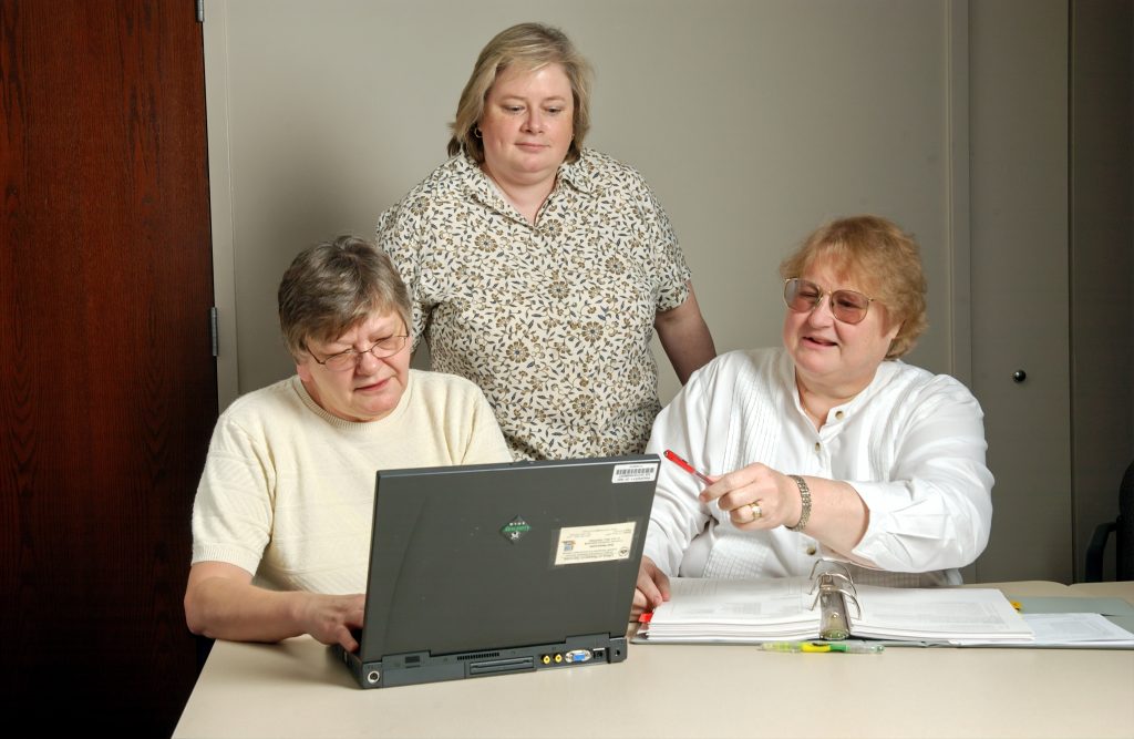 Three older women looking together at a computer, possibly playing Staying Sharp games by AARP.org
